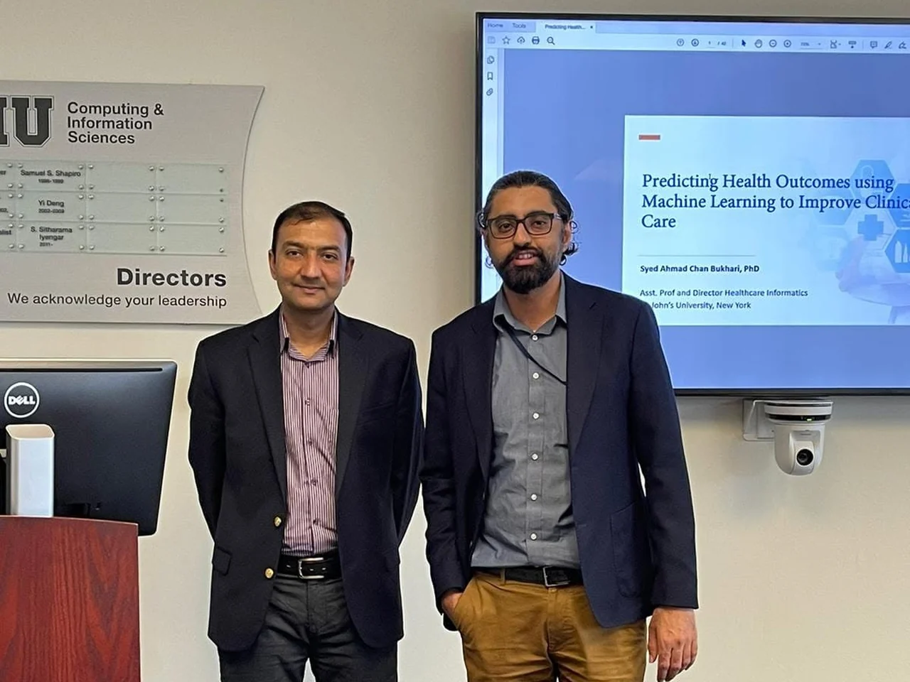 Dr. Bukhari standing with a colleague beside a presentation on predicting health outcomes with machine learning.